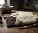 An open wrapper exposing dark Charas Cannabis Infused Chocolate Bars next to a small jar of charas resin on a rustic wooden table.