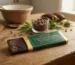 A premium Delta 8 Chocolate Bar partially unwrapped in gold foil with topofficialgenetics.co.uk branding on a rustic wooden table.